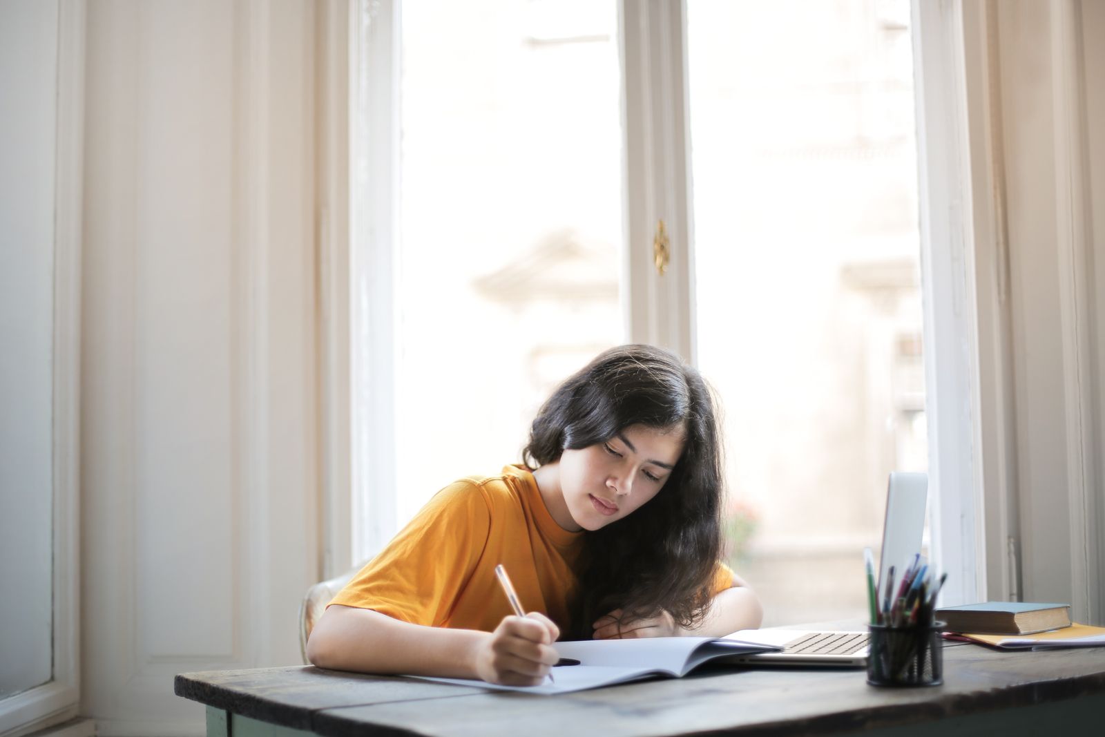 A teenager focused on homework at a desk in warm daylight